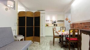 A compact living space with a sofa, dining table, and chairs, a kitchen area with a brick wall, and a decorative partition. - JOIVY Calm 1-bed flat (Lisbon)