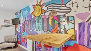 A room with a colorful mural, a wooden table, a red chair, and a bed with striped bedding.