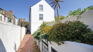 A narrow alleyway with a white building on the right, a palm tree, and dense greenery.