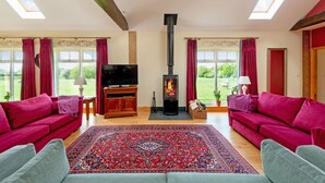 A living room with two red sofas, a large red and blue patterned rug, a TV, and a wood-burning stove. - Cart House 2 bedrooms - sleeps 4-5 guests  in 2 bedrooms (Beverley)