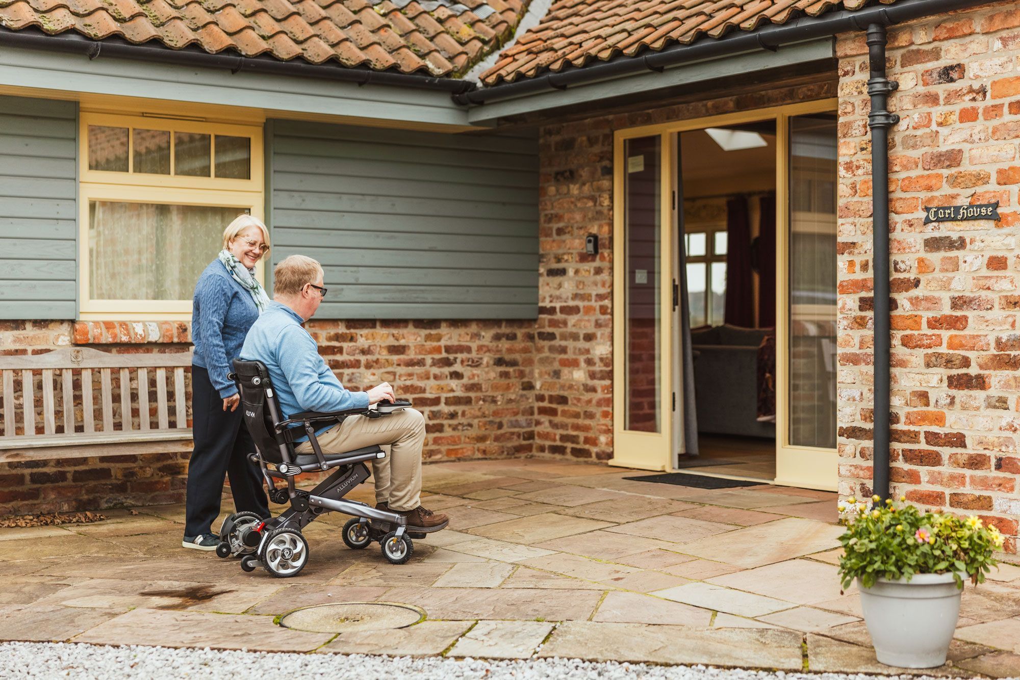 A brick building with a tiled roof, a wheelchair, and a person pushing it.