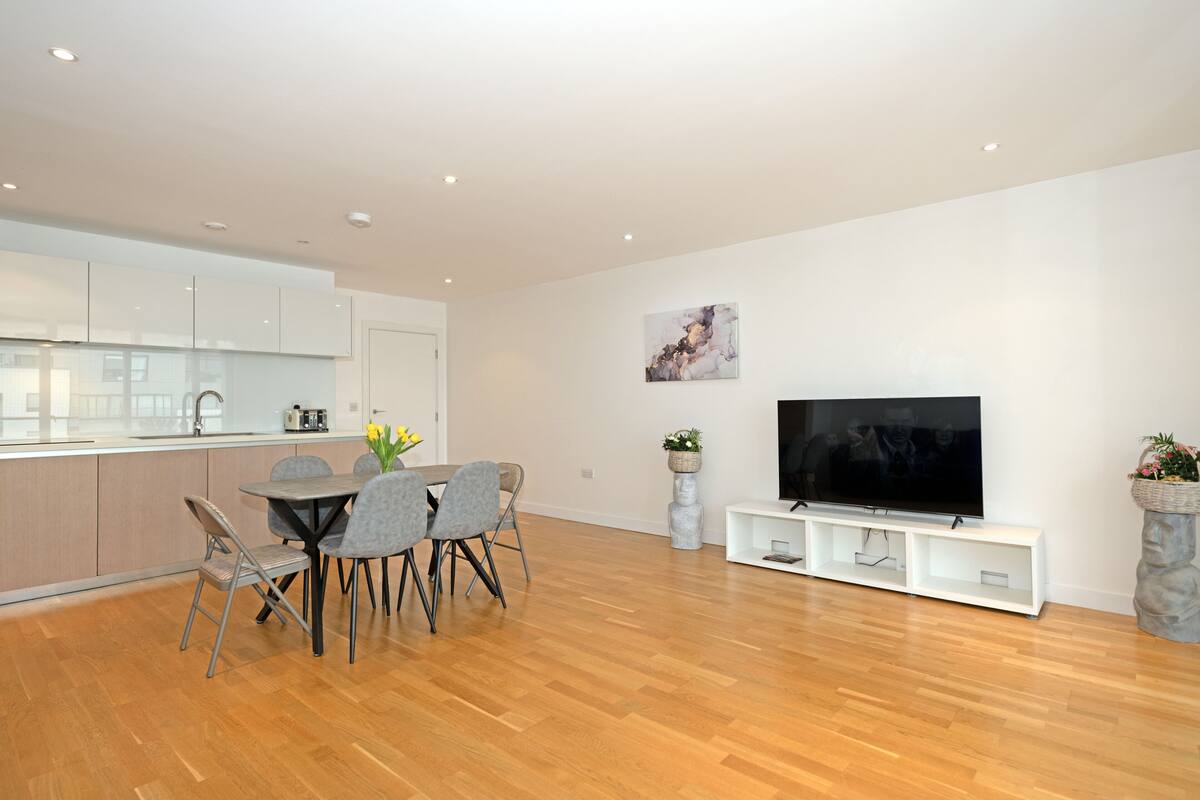 A modern living room with a dining area, wooden flooring, a flat-screen TV, and minimalist decor.