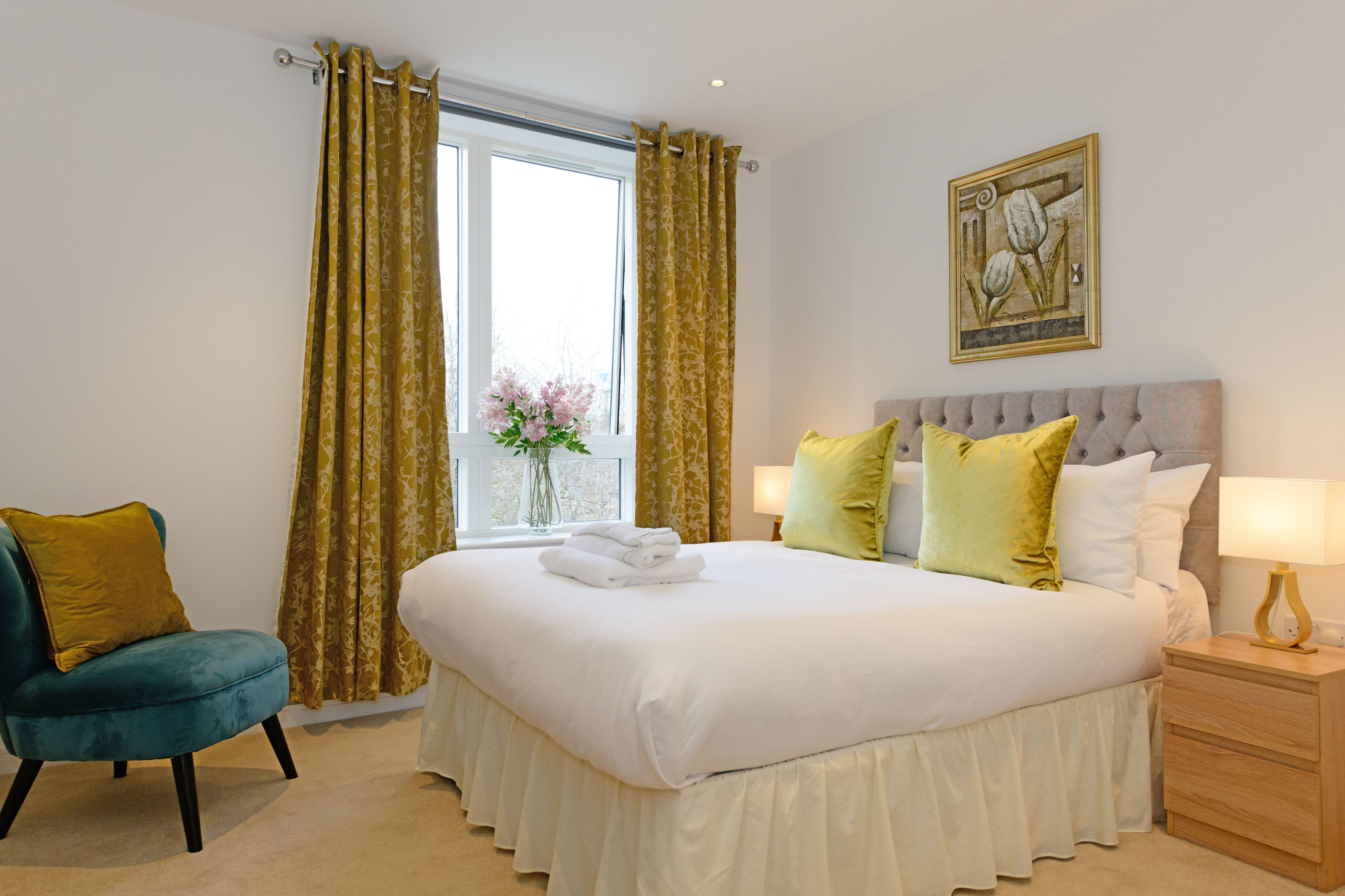 A neatly arranged bedroom with a large bed, a chair, a nightstand, and a window with curtains.