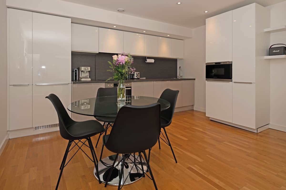 A modern kitchen with white cabinets, a glass dining table, and black chairs.