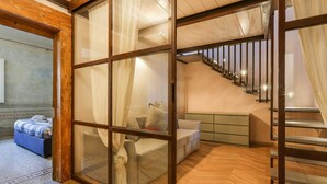 A modern hotel room with a wooden floor, a bed with a blue and white striped bedspread, a white sofa, and a staircase with a metal railing. - Belle Arti' Stunning Apartment (Florence)
