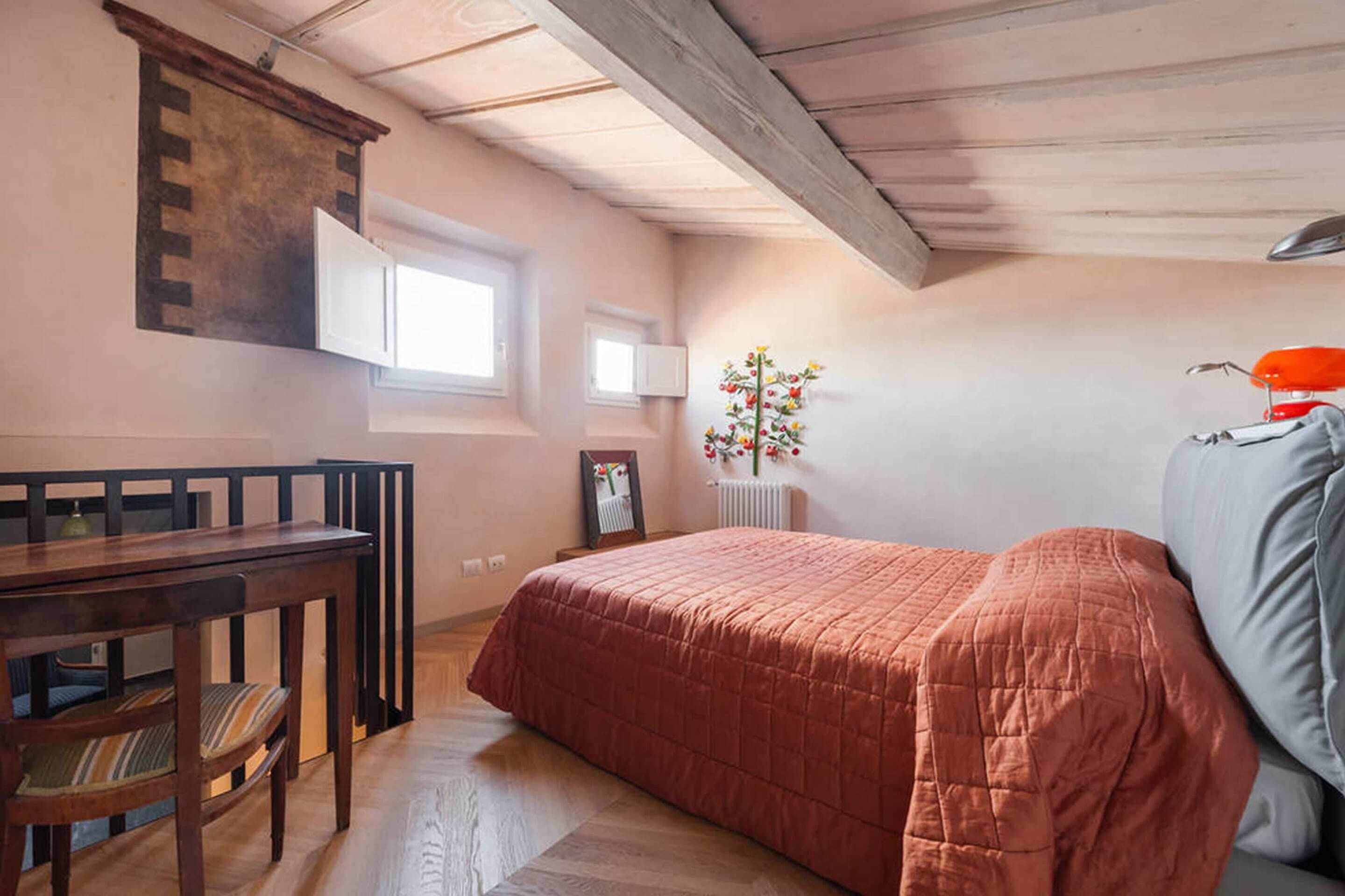 A bedroom with a wooden bed, a desk, and a chair. There is a window and a radiator with flowers.