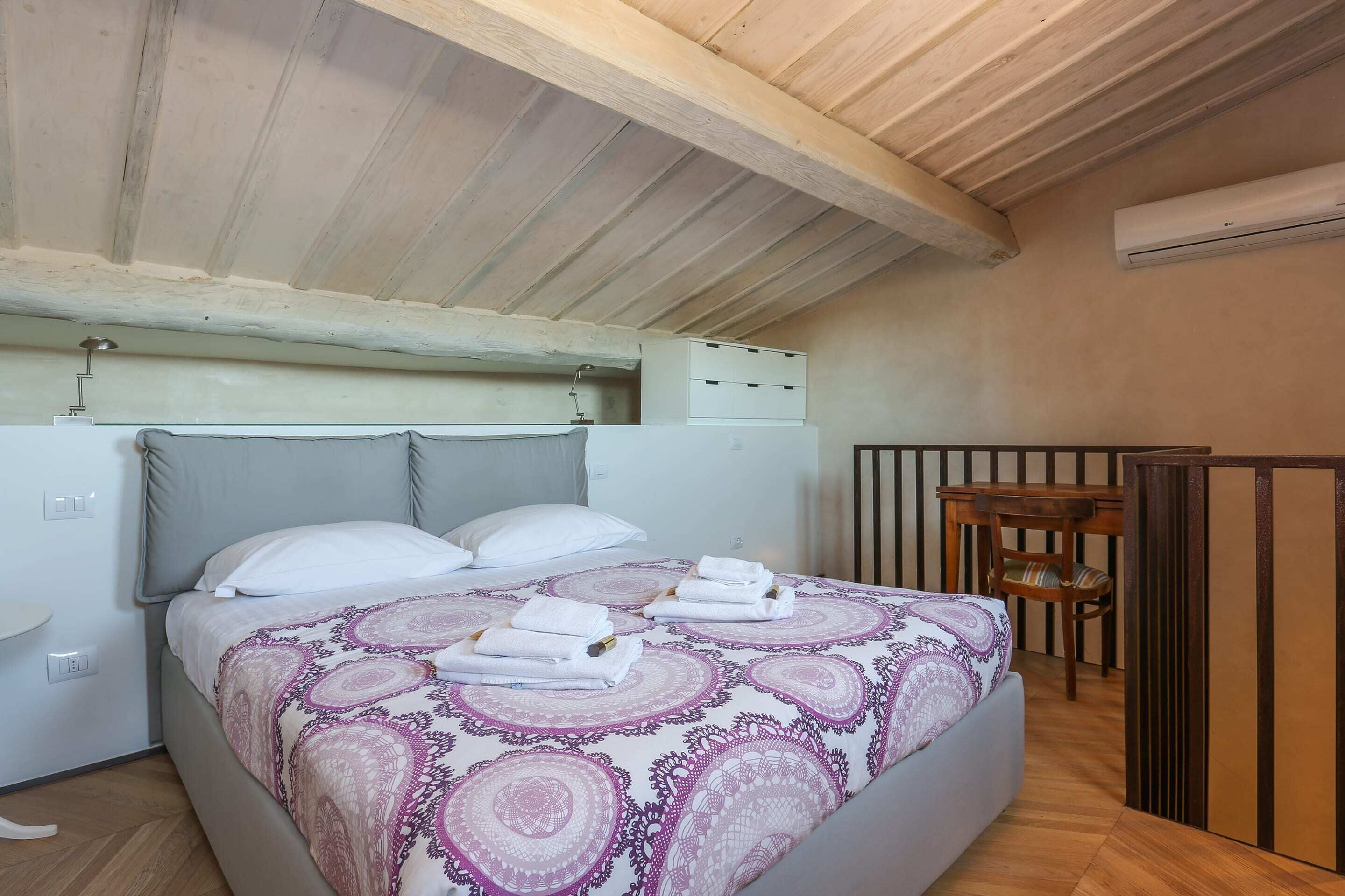 Une chambre à coucher comprenant un lit, des oreillers, une table de chevet, un bureau et un appareil de climatisation.