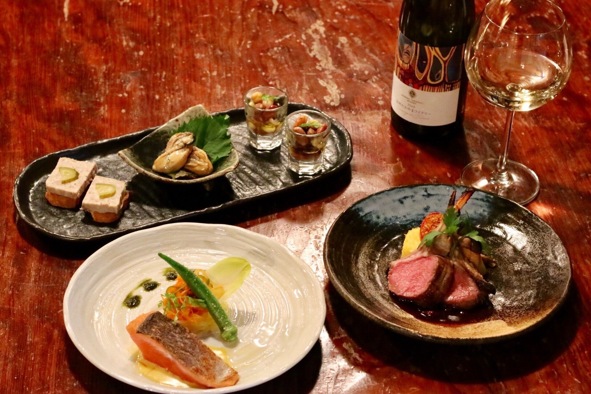 Una mesa con tres platos, una botella de vino y una copa de vino.