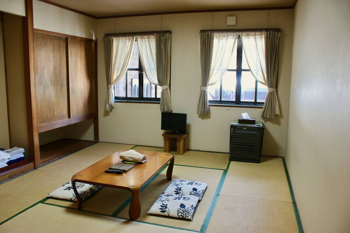 A traditional Japanese room with tatami flooring, a low wooden table, a television on a small stand, and a cabinet.