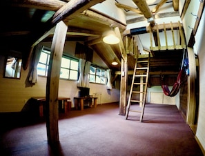 A rustic room with wooden beams, a loft bed, a ladder, and a hammock. - Spa Lodge Redwood Inn (Takayama)