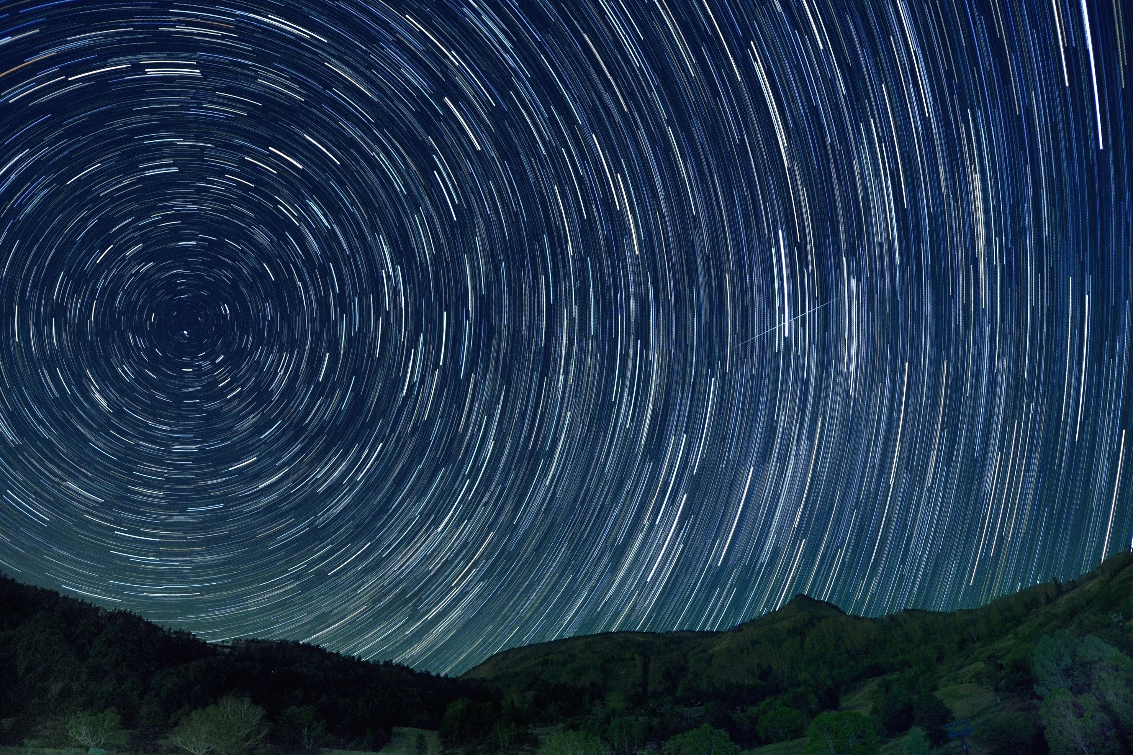 A star trail photograph of a mountainous landscape at night.