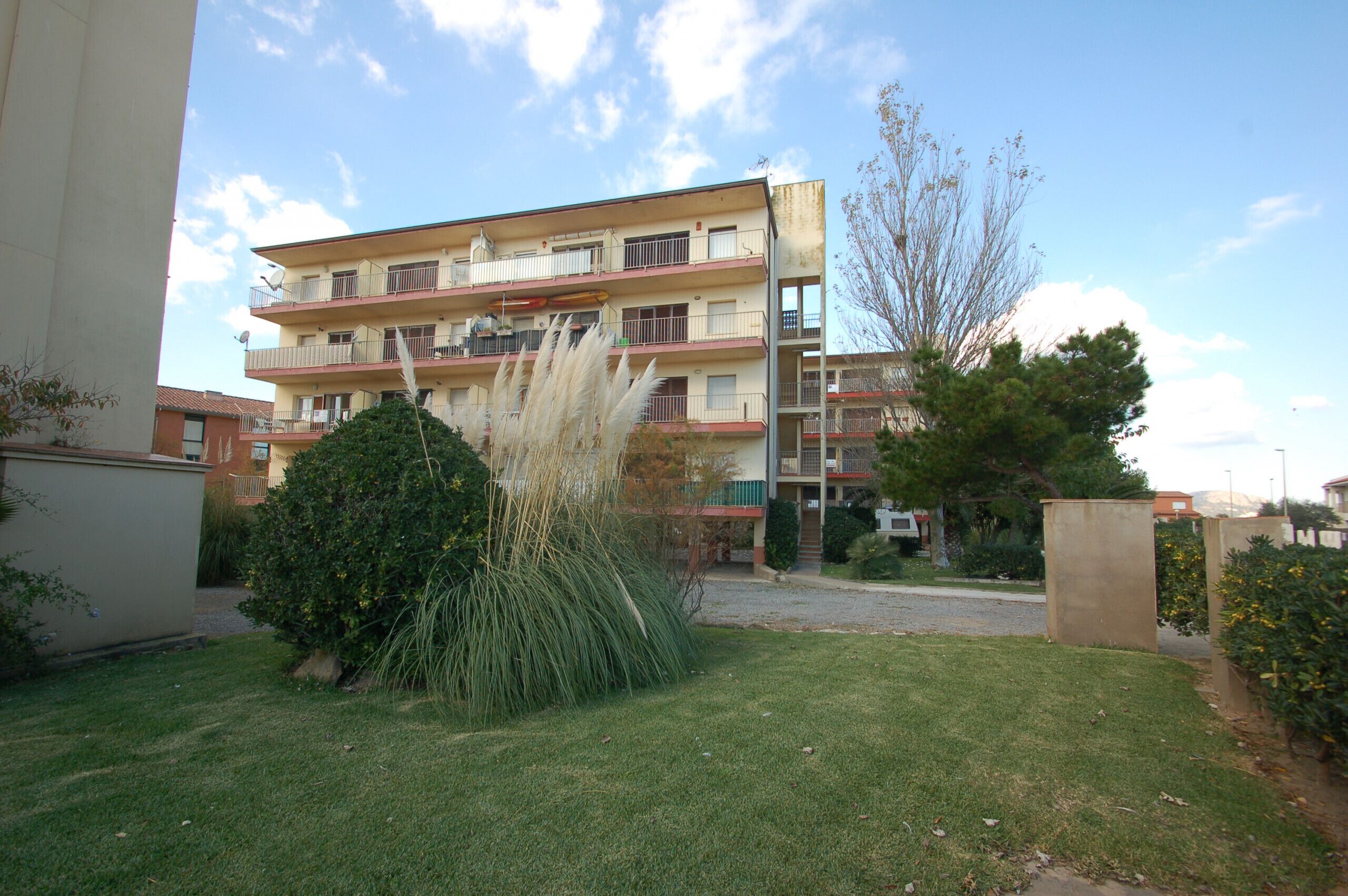 A multi-story residential building with balconies, a well-maintained lawn, and a clear sky.