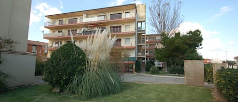 A multi-story residential building with balconies, a well-maintained lawn, and a clear sky.