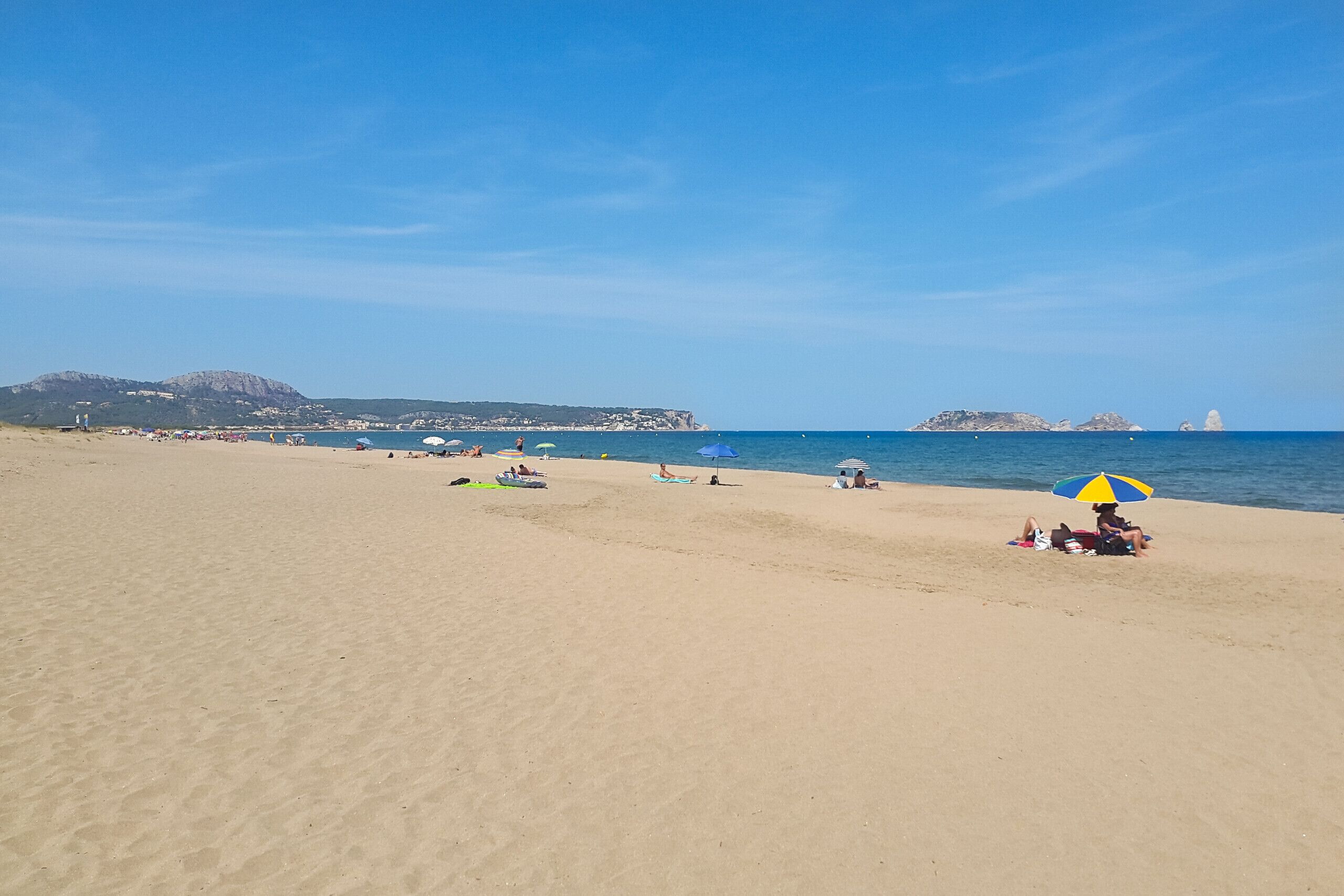 A beach with people relaxing, umbrellas, and boats.