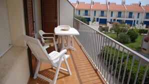 A balcony with a white table and two white chairs, a wooden door, and a view of a residential area with buildings and greenery. - Mare Nostrum 2D 324 - Close to the beach, modern (Torroella de Montgri)