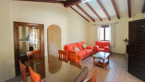 A dining area with a wooden table and chairs, a red sofa, and a dark wooden door. - Santa Ana - pretty holiday property with garden and private pool in Benissa (Benissa)
