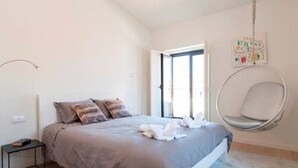 Un dormitorio con cama, mesita de noche, sillón colgante y ventana.