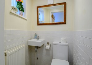 Bathroom features a pedestal sink, toilet, and mirror with a shelf for personal items.