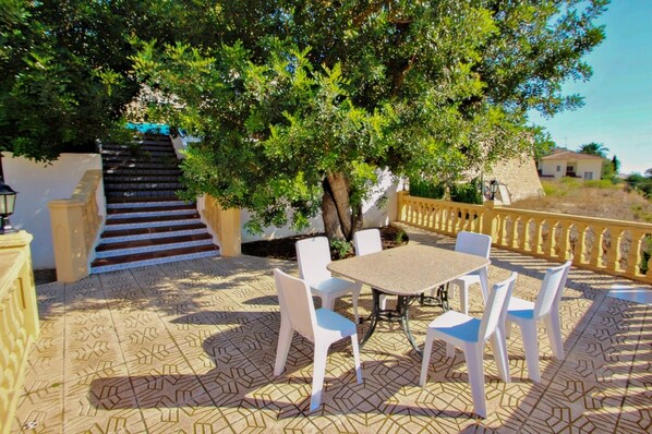 Eine Terrassesituation mit Tisch, Stühlen, einem Baum und einer Treppe.