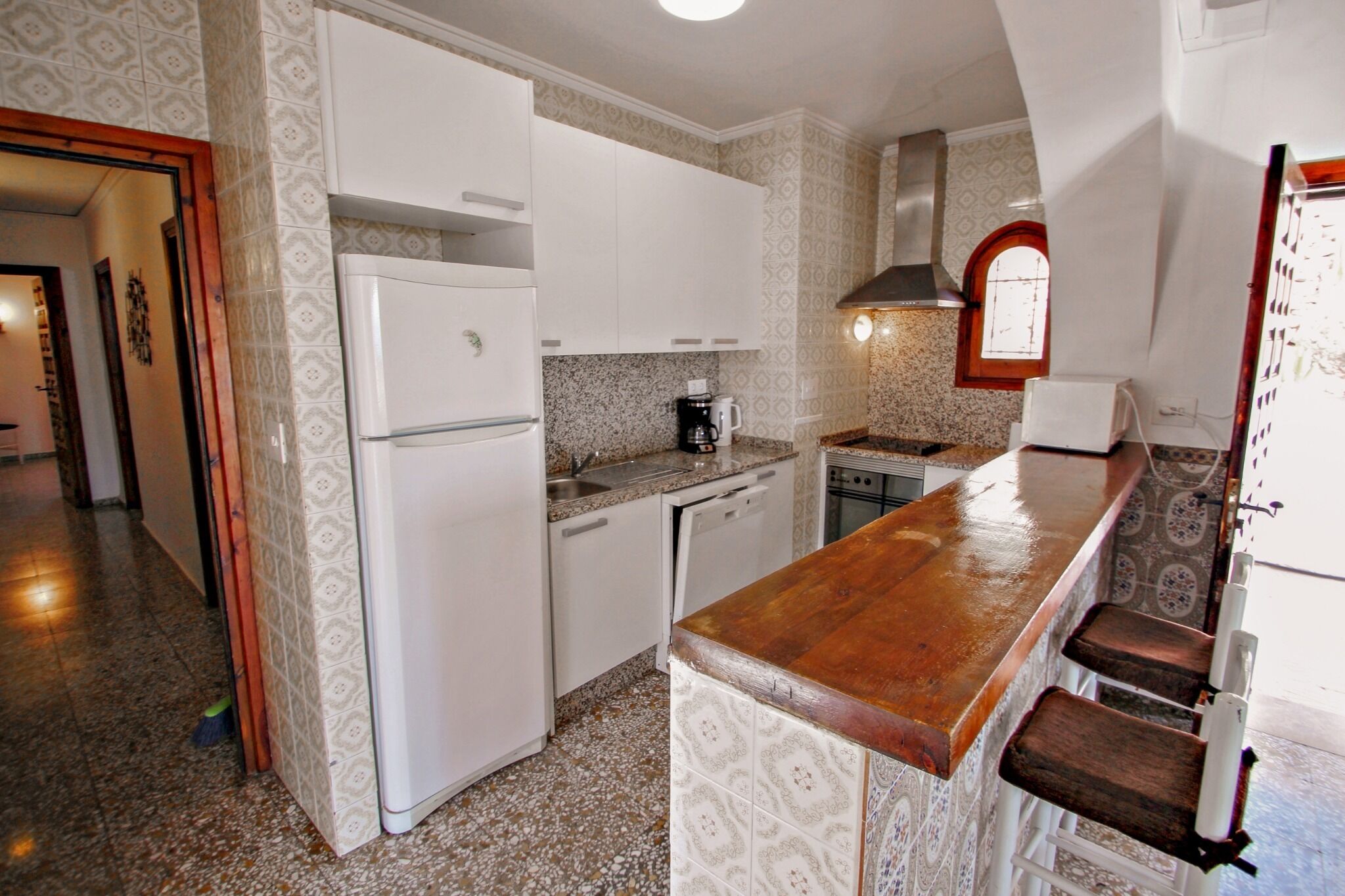 Una cocina compacta con armarios blancos, una encimera de madera y una estufa empotrada.
