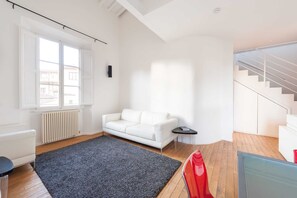 Una sala de estar moderna con un sofá blanco, un tapete oscuro y una escalera a la derecha.