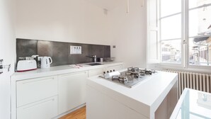 Ett modernt kök med vita köksskåp, en gasspis, en vattenkokare och ett fönster med utsikt över gatan.