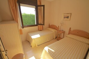 Quarto com duas camas de solteiro, uma mesinha de cabeceira com abajur, uma janela com cortinas e um quadro na parede.