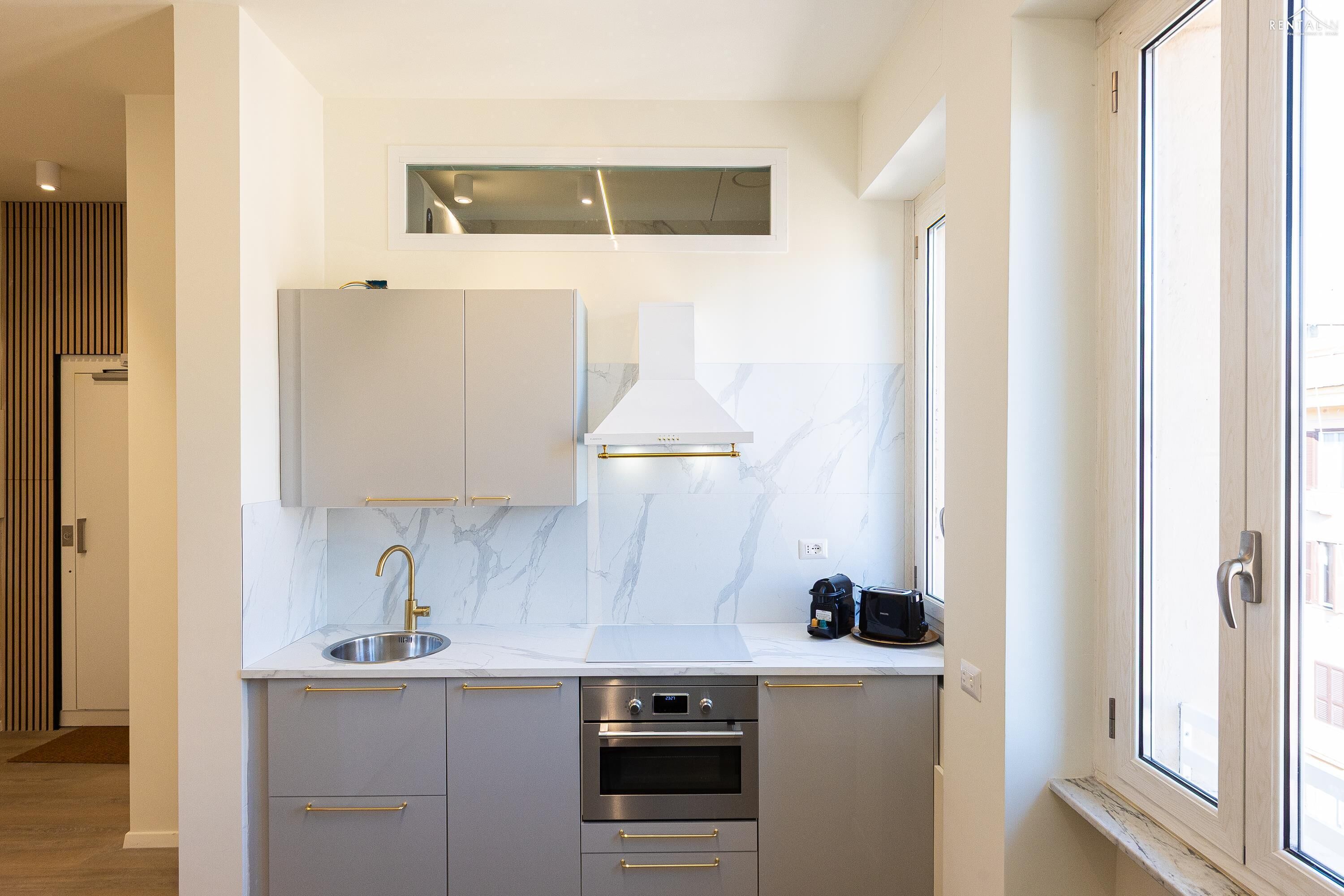 A modern kitchen with a stainless steel sink, a built-in oven, and a window with a view of the city.