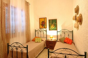 A bedroom with two single beds, a nightstand with a lamp, and two framed floral pictures on the wall. - Villa Contrada  - Holiday Rental by the Sea with swimming pool in Scopello, Sicily (Scopello)
