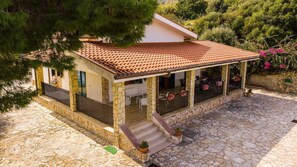 A stone house with a tiled roof, a covered porch with outdoor seating, and a stone staircase leading to the entrance. - Villa Contrada  - Holiday Rental by the Sea with swimming pool in Scopello, Sicily (Scopello)