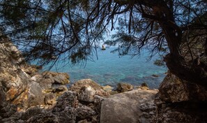 A rocky coastal landscape with clear blue sea and a sailboat in the distance. - Villa Contrada  - Holiday Rental by the Sea with swimming pool in Scopello, Sicily (Scopello)