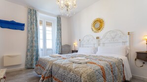 A bedroom with a large bed, a chandelier, a mirror, and a window with curtains.