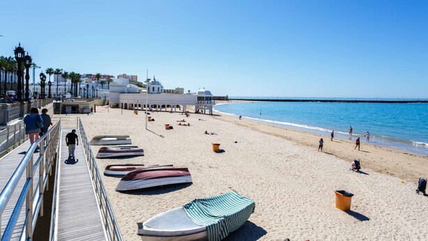 A beach with a wooden walkway, several boats, and a clear blue sky.