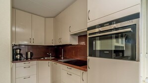 Una cocina compacta con armarios blancos, horno integrado y cafetera.