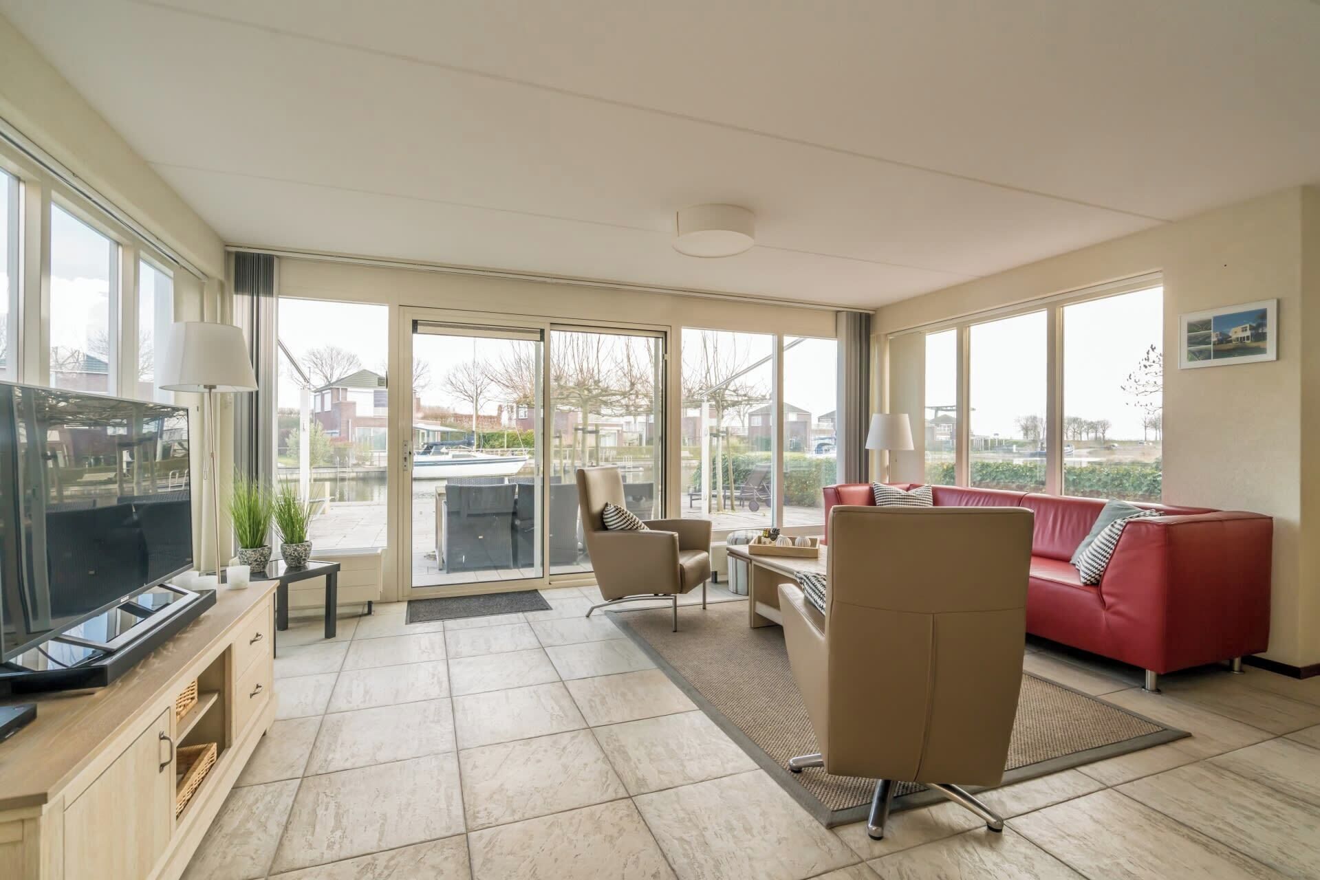 A spacious living room with a red sofa, a TV, and a large window overlooking a garden.