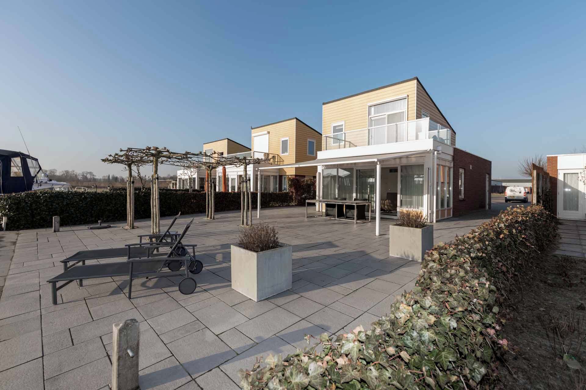 Una zona residencial moderna con un patio, mobiliario exterior y un espacio cubierto con mesa y sillas.