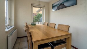 Un comedor con una mesa de madera, sillas de mimbre, una lámpara colgante, una ventana con persianas y un cuadro en la pared.