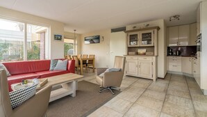 Un espacio habitable compacto con un sofá rojo, una mesa de centro de madera, una mesa de comedor con sillas, una zona de cocina con armarios y un ventanal grande.
