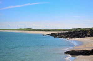 A beach with clear blue water, sandy shore, and rocky outcrops.