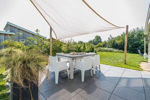 Un patio con una mesa y sillas, rodeado por un dosel blanco, y una casa al fondo.