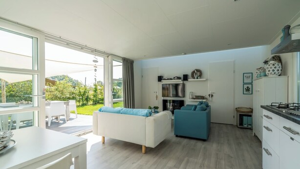 Un salon moderne comprenant un canapé, un téléviseur et un coin cuisine avec des placards et une cuisinière.