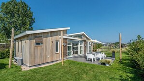Una casa moderna con facciata in legno, ampie vetrate e una zona patio con mobili da esterno.