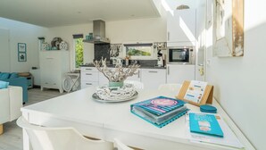 Una cucina moderna con mobili bianchi, un'area pranzo con tavolo bianco e vista sull'esterno.