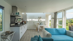 Una cucina moderna con mobili bianchi, un'area pranzo con tavolo e sedie bianche, e un divano blu in una stanza luminosa con ampie finestre.