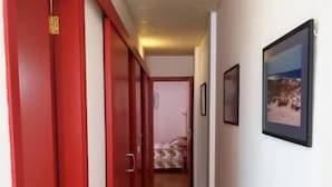 Un pasillo con puertas rojas, suelo de baldosas y cuadros en las paredes.