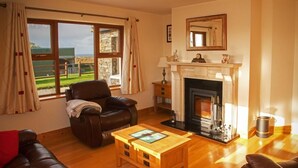 Ein Wohnzimmer mit Kamin, Ledersofa, Couchtisch aus Holz und großen Fenstern mit Vorhängen.