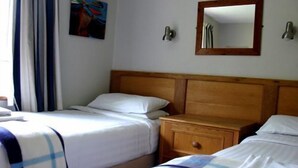 A hotel room with two single beds, a wooden nightstand, a mirror, and a painting on the wall.