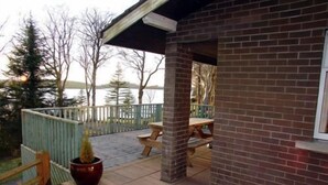 A brick building with a covered patio area, a wooden deck, and a view of a lake.