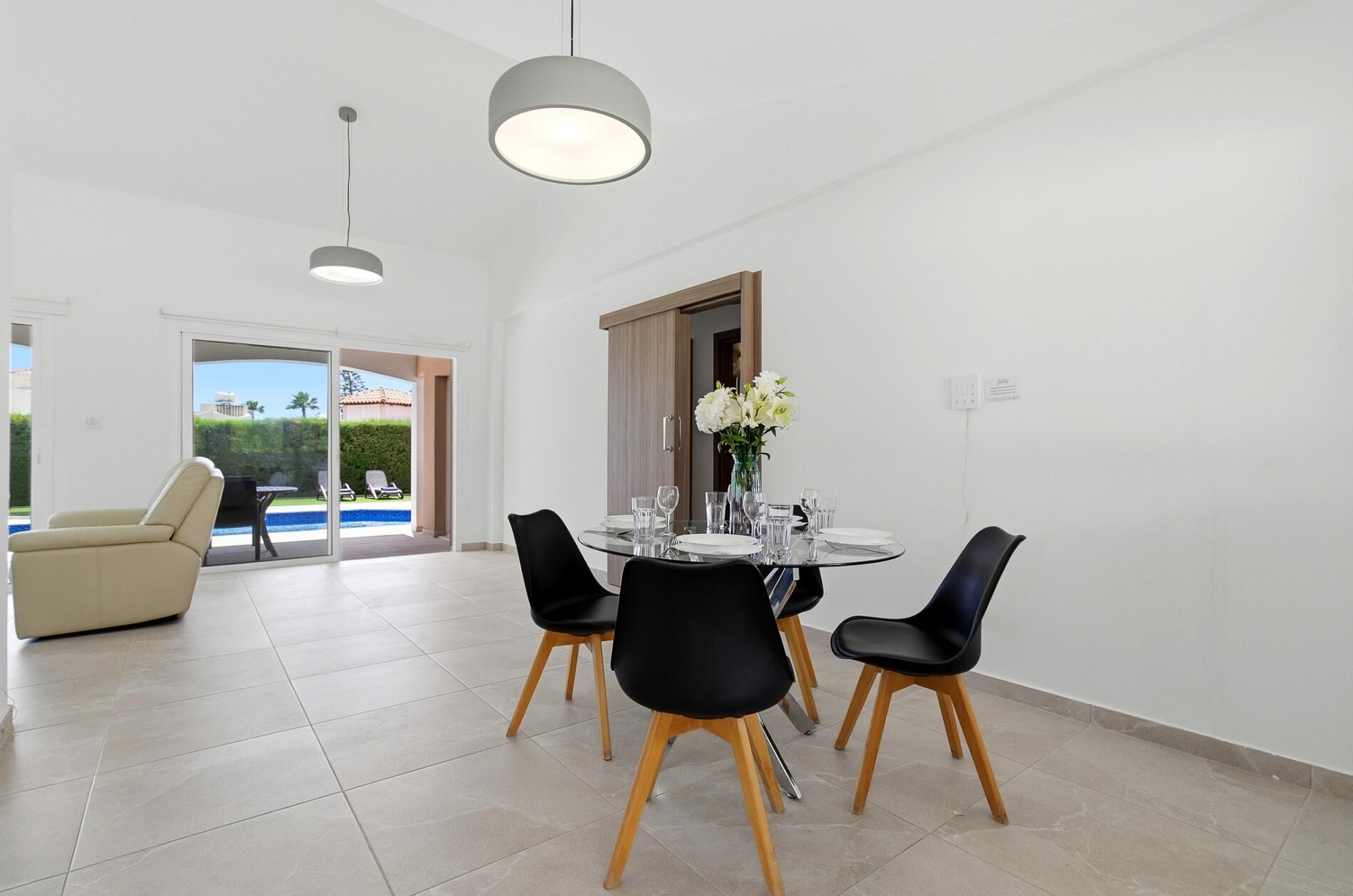 A dining area with a round table, black chairs, and a vase of flowers.
