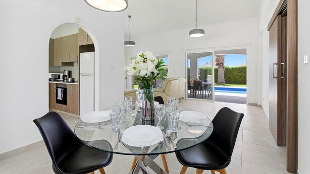 Un coin repas avec une table en verre, des chaises noires et un vase de fleurs.